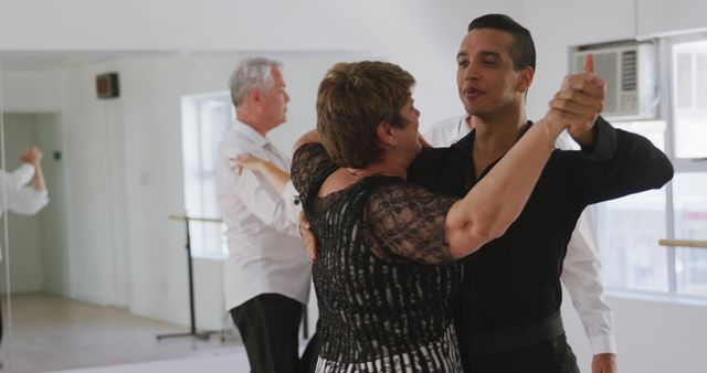 Focused diverse male dance teacher dancing with mature woman at ballroom dance class, copy space. Dance, teaching, learning, hobbies and active senior lifestyle, unaltered.