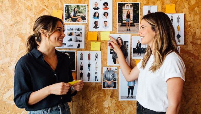 Creative team reviewing fashion moodboard and sticky notes on chipboard wall