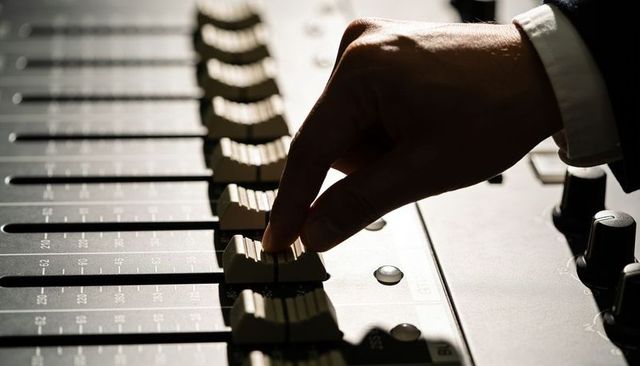 Adjusting mixer fader close-up, sound engineer hand controlling levels with suit cuff