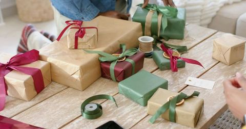 Diverse couple wrapping and tying ribbons on kraft-wrapped rustic holiday gifts