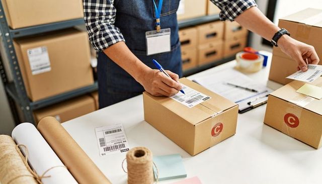 Warehouse worker labeling packages at packing station using barcode labels and packing tape