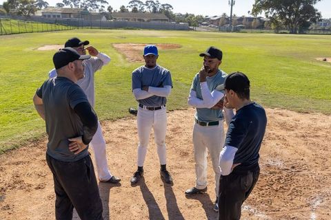 Diverse baseball team discussing strategy on pitcher's mound, teammates in uniforms