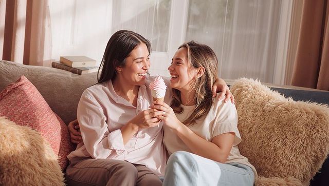 Couple sharing soft-serve ice cream on cozy sofa embracing tender moment in sunlit room