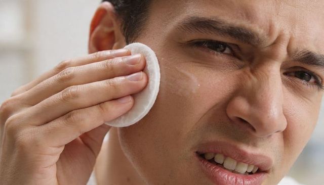 Man removing facial cream with cotton pad at bathroom vanity closeup grooming routine
