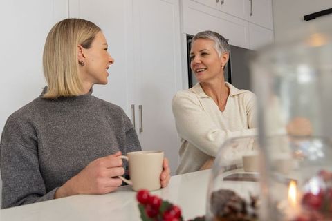 Mature woman and younger woman chatting over coffee at cozy modern kitchen island