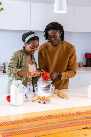African american couple baking together in bright modern kitchen sifting flour