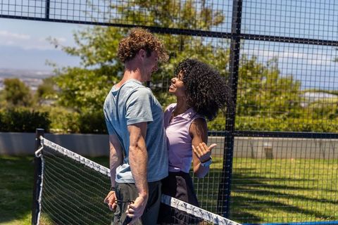 Young couple flirting at net during outdoor racket sport match on sunny grass court