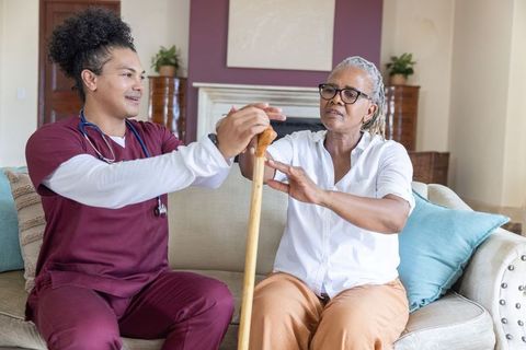 Home caregiver assisting senior african american woman with cane for mobility and independence