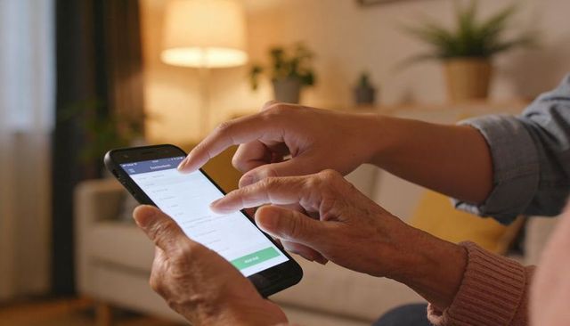 Helping Senior Using Smartphone with Caregiver Guiding Touchscreen in Cozy Living Room