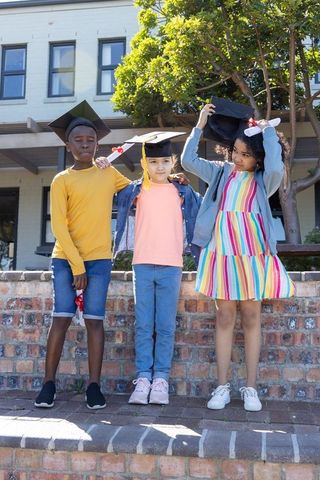 Diverse kids celebrating elementary graduation wearing caps and holding diplomas