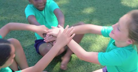 Teen girls joining hands in team huddle on sunlit field showing unity and teamwork