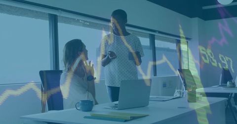 Mid-adult colleagues collaborating over financial charts with laptop and smartphone in modern office