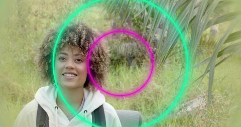 Curly-haired woman hiking with backpack and neon light rings in lush green park trail