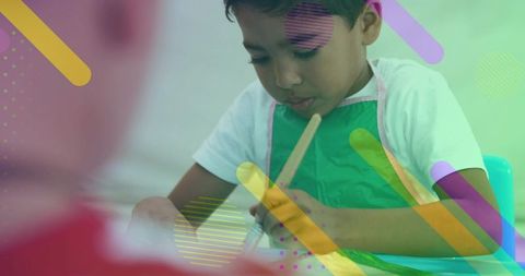 Young boy painting at table wearing green apron focusing on art and creativity
