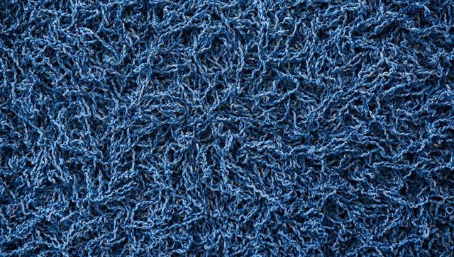 Macro close-up blue shag rug showing twisted yarn and dense tufts, textile texture