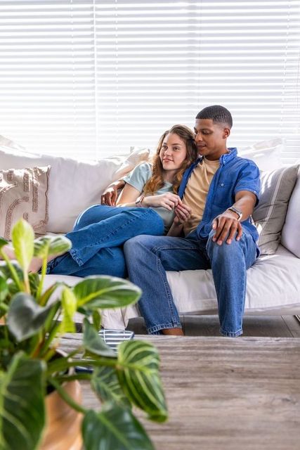 Interracial couple relaxing and cuddling on sofa in bright modern living room