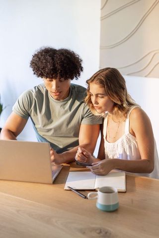 Young couple collaborating on laptop and smartphone at home desk planning finances budget
