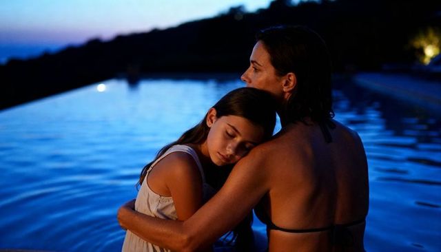 Mother hugging daughter at infinity pool dusk conveying tender protection and tranquility