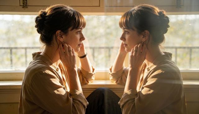 Woman gazing at window reflection during golden hour wearing beige shirt and hoop earrings