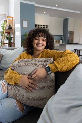 African american woman relaxing on sofa hugging pillow wearing smartwatch in modern home