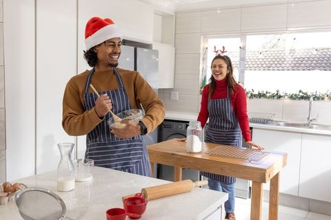 Couple making Christmas cookies in bright kitchen with Santa hat and reindeer antlers