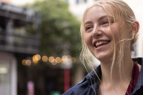 Young blonde woman smiling under bistro lights wearing denim jacket and burgundy top