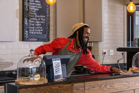 Smiling african american barista wiping counter in cozy urban cafe with qr checkout