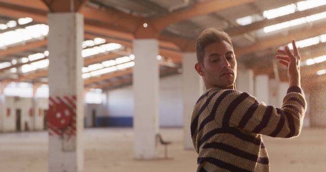 Shows young man performing passionate dance in an abandoned warehouse. Open space and industrial backdrop, suitable for themes of creativity, urban exploration, performing arts, personal expression, street dance. Great for ads, promotional materials, websites, visual content on art or dance-related topics.