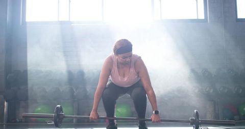 Mid-adult african american woman performing barbell deadlift under dramatic backlit light