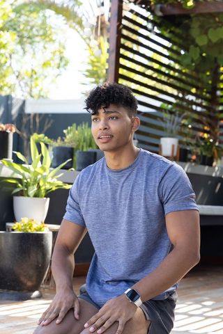 African american man sitting on deck among potted plants wearing blue tee and smartwatch