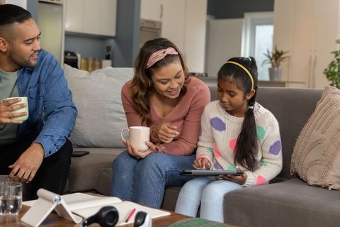 Multicultural family bonding while daughter learning on tablet with parents watching on sofa