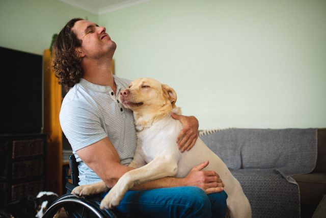 Disabled man sitting in wheelchair hugging his Labrador dog in a cozy living room. Ideal for use in articles or advertisements about disability, companionship, emotional support animals, and the bond between humans and pets.