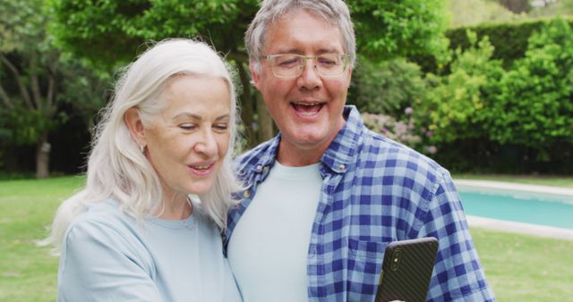 Image of caucasian senior couple embracing in garden, taking selfie. retirement lifestyle, spending quality time with friends.