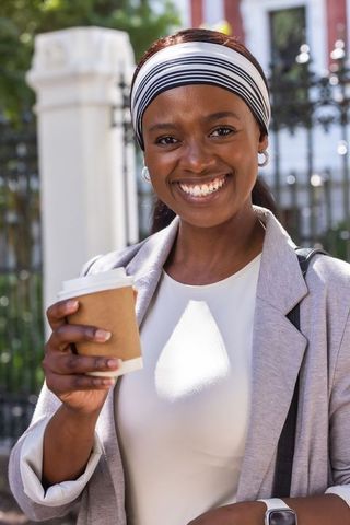 Smiling woman holding takeaway coffee wearing gray blazer headband urban portrait