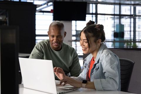 Diverse coworkers collaborating on laptop in modern open-plan office