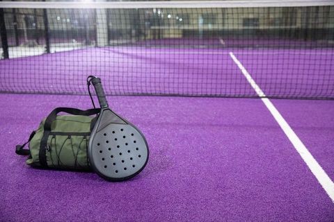 Padel paddle resting on duffel bag on vibrant purple court beside net with white line