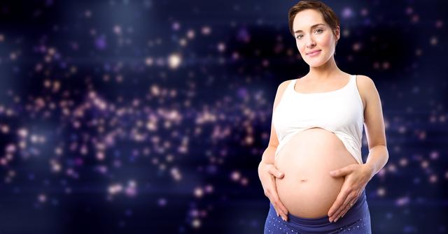 Digital composition of pregnant woman standing with hands on stomach against illuminated background