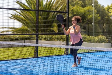 African american woman celebrating while playing padel on vibrant blue outdoor court