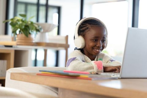 African american girl learning online wearing headphones using laptop in bright home