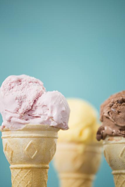 Close-up of a strawberry ice cream cone with vanilla and chocolate ice cream cones blurred in the background. Perfect for use in food blogs, dessert menus, summer promotions, and advertisements for ice cream parlors.