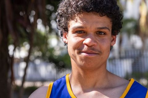 Young african american man smiling outdoors wearing blue athletic tank with yellow trim