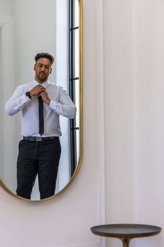African man adjusting black tie in oval gold mirror preparing for work