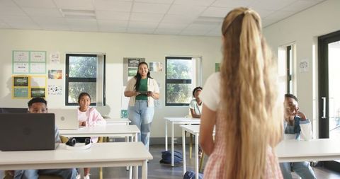 Teacher guiding teenage students during classroom presentation with tablet and laptops