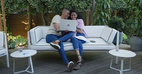 Diverse Couple Relaxing on Garden Sofa with Laptop