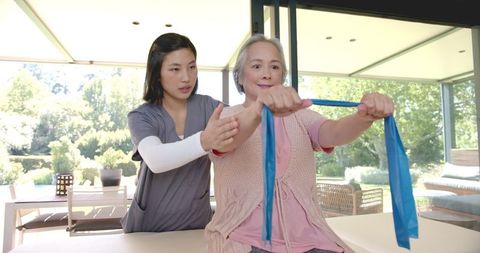Senior Asian Woman Doing Resistance Band Exercises with Physical Therapist