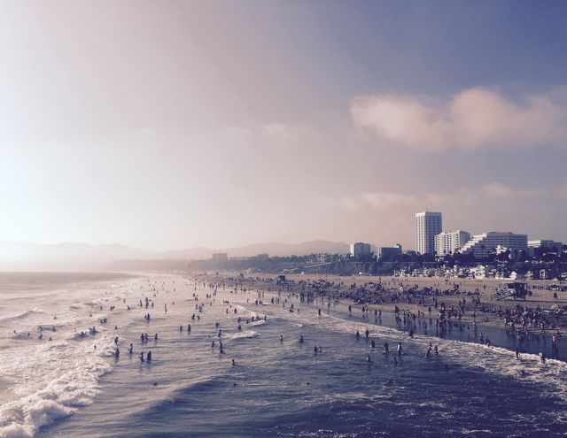 People enjoying a sunny day at the beach with ocean waves, city skyline, and mountains in the background. Suitable for travel blogs, vacation advertisements, and urban coastal themes.
