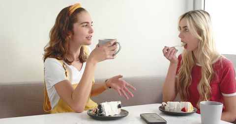 Two friends chatting over coffee and cake in sunlit home nook, cozy casual conversation