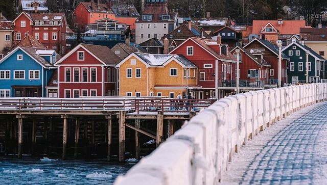 Colorful wooden harbor houses lining snowy pier over icy water, winter coastal town