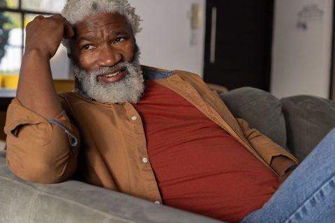 Relaxed african american senior reclining on sofa smiling in cozy home with soft light