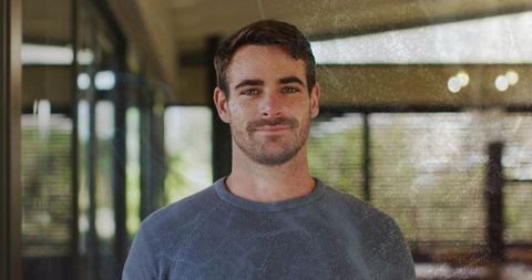Confident young man standing indoors by glass panels with soft natural daylight